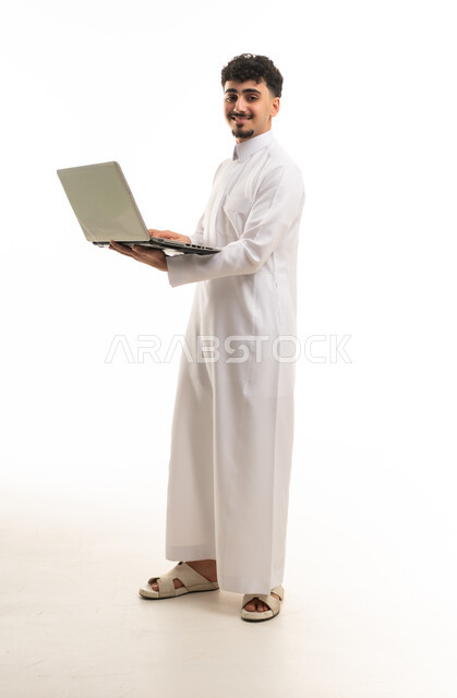 رجل سعودي بالثوب التقليدي يحمل جهاز كمبيوتر محمول