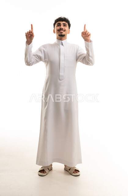شاب سعودي يرتدي الثوب الأبيض ويشير للأعلى بخلفية بيضاء