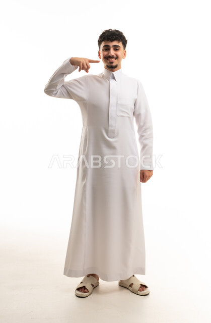 شاب سعودي بالثوب الأبيض يبتسم ويشير لوجهه