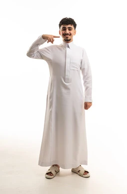 شاب سعودي بالثوب الأبيض يبتسم ويشير لوجهه