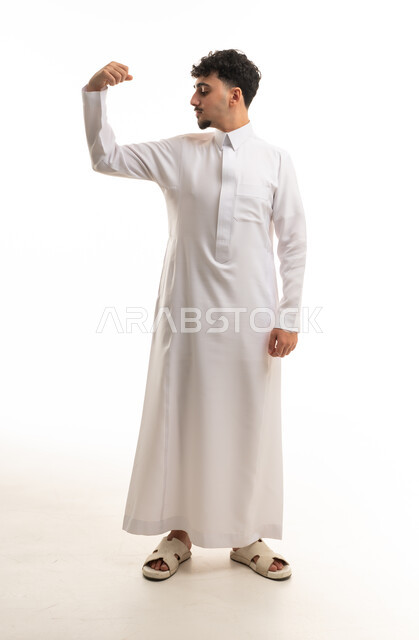 شاب سعودي بالثوب الأبيض يستعرض عضلاته في الاستوديو