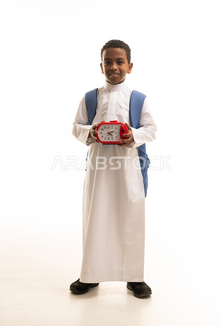 طالب مدرسي سعودي يحمل ساعة منبه وحقيبة