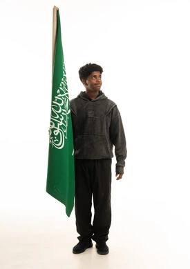 شاب سعودي يقف بجانب علم المملكة العربية السعودية
