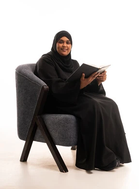امرأة سعودية تجلس وتقرأ كتاباً في خلفية بيضاء