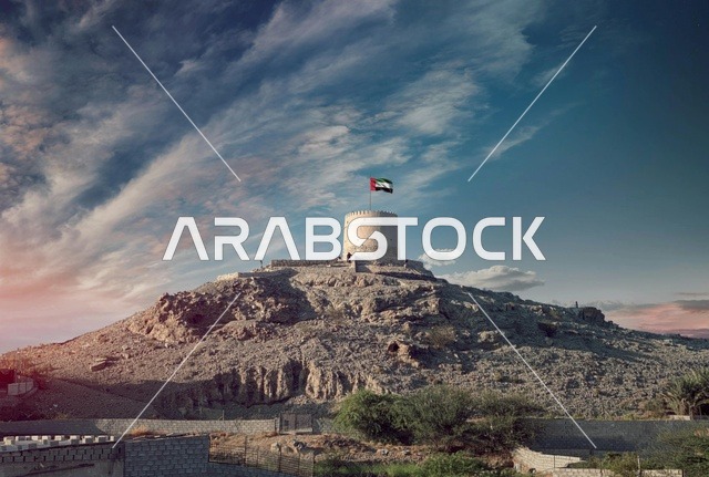 علم الإمارات فوق حصن جبلي تقليدي قديم وقت الغروب