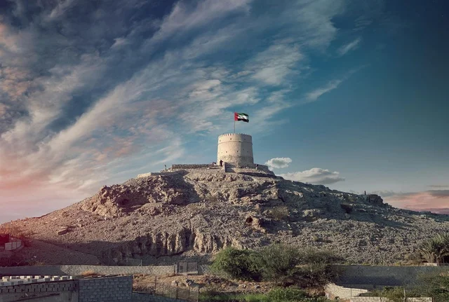 علم الإمارات فوق حصن جبلي تقليدي قديم وقت الغروب