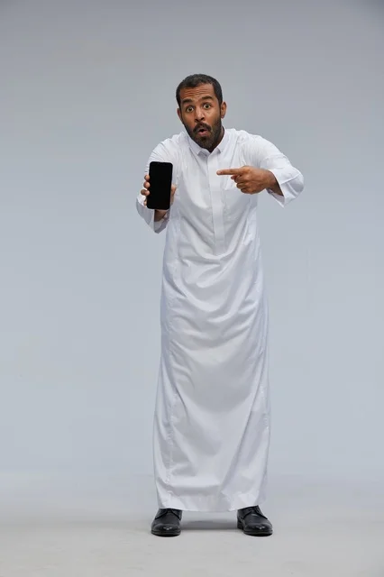 رجل سعودي بالثوب الأبيض يشير لشاشة هاتف ذكي