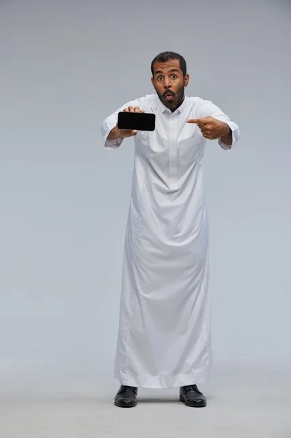 Saudi Man in White Thobe Pointing at Smartphone Screen