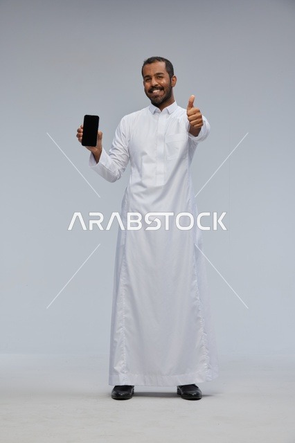 Saudi Man in White Thobe Holding Smartphone Thumbs Up