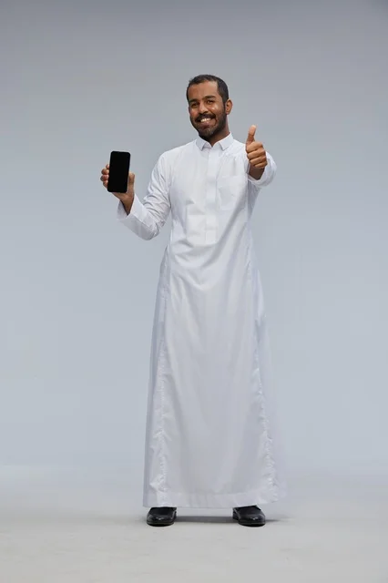 رجل سعودي بالثوب الأبيض يمسك هاتفاً ذكياً مع إشارة الإبهام