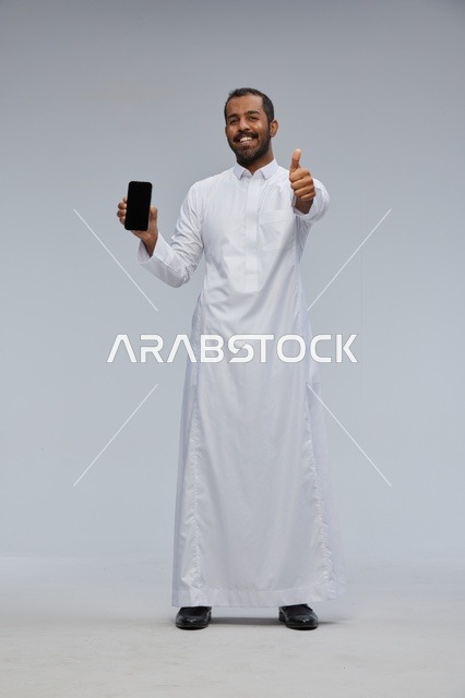 Saudi Man in White Thobe Holding Smartphone Thumbs Up