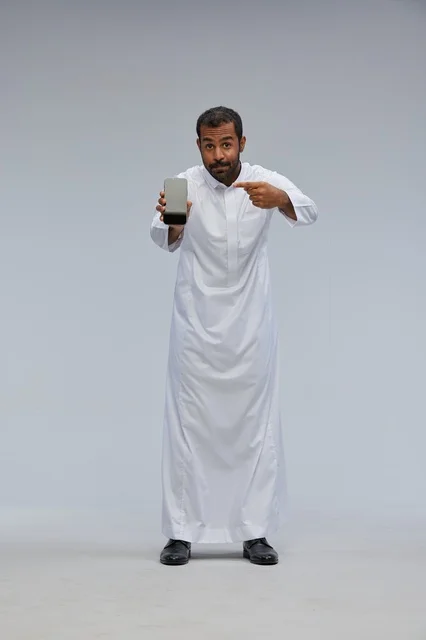 Saudi Man in White Thobe Pointing at Smartphone Screen