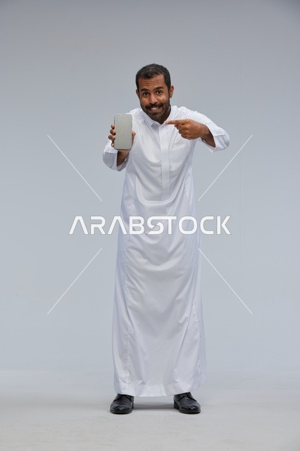 رجل سعودي بالثوب الأبيض يشير لشاشة هاتف ذكي
