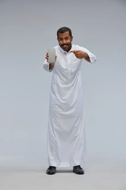 رجل سعودي بالثوب الأبيض يشير لشاشة هاتف ذكي
