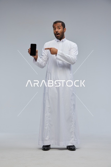 Saudi Man in White Thobe Pointing at Smartphone Screen