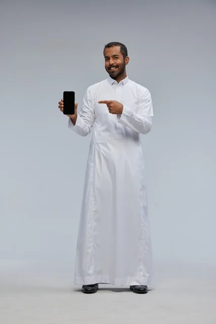 رجل سعودي بالثوب الأبيض يشير إلى شاشة هاتف ذكي