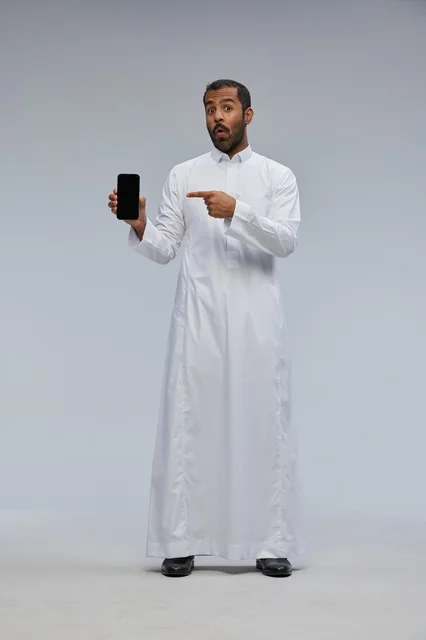 Saudi Man in White Thobe Pointing at Smartphone Screen
