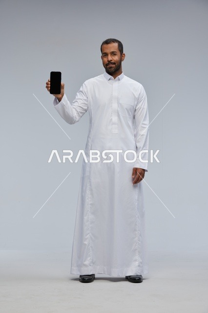 رجل سعودي بالثوب الأبيض يعرض شاشة هاتف ذكي