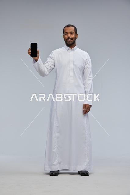 Saudi Man in White Thobe Holding Smartphone Screen