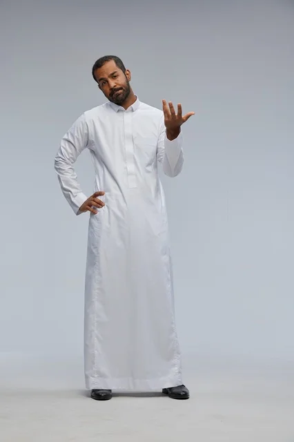 رجل سعودي بالثوب الأبيض يلوح بيده أمام خلفية رمادية