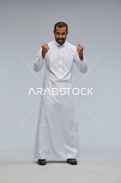 رجل سعودي يرتدي الثوب الأبيض ويحتفل بنجاحه في الاستوديو