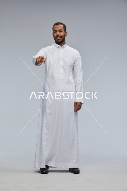 رجل سعودي بالثوب الأبيض يشير نحو الكاميرا في استوديو