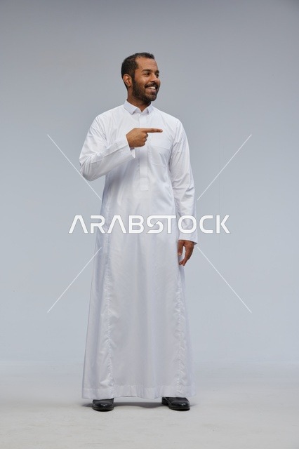 Saudi Man in White Thobe Pointing Against Grey Background