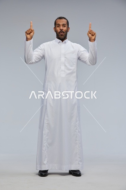 رجل سعودي بالثوب الأبيض يشير للأعلى في الاستوديو