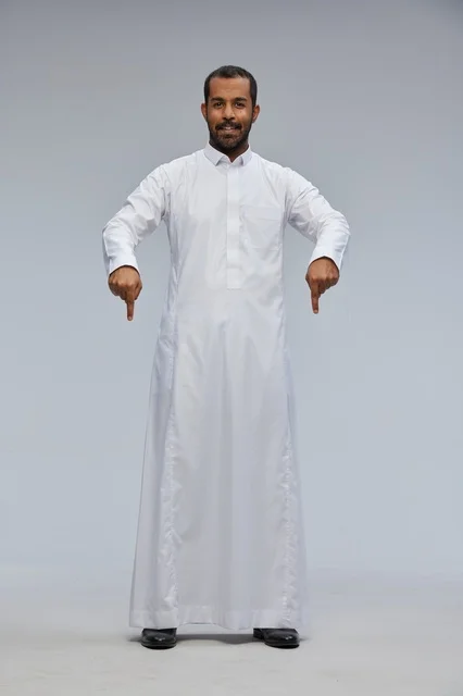 رجل سعودي يرتدي الثوب الأبيض يشير للأسفل في استوديو