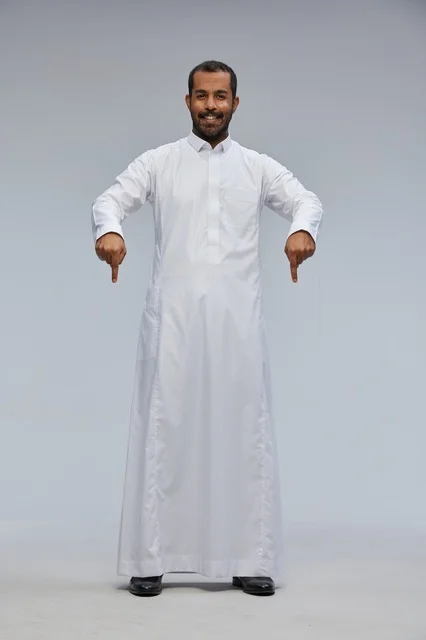 رجل سعودي بالثوب الأبيض يشير للأسفل بخلفية رمادية