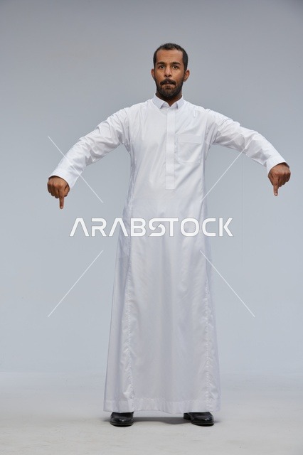 رجل سعودي بالثوب الأبيض يشير إلى الأسفل في استوديو