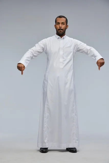 رجل سعودي بالثوب الأبيض يشير إلى الأسفل في استوديو