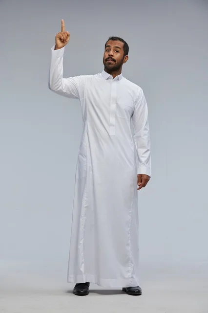رجل سعودي يرتدي ثوباً أبيض يشير للأعلى في استوديو
