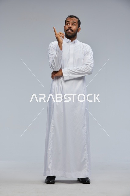 رجل سعودي بالثوب الأبيض يشير للأعلى بخلفية رمادية