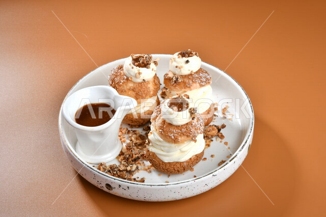 طبق من الحلا البارد مزين بالكريمة وجانبه صوص الشوكولاته ، حلا شرقي ، حلويات رمضانية ، حلويات وسكريات ، قطع الحلوى الشهية ، التحلاية ، حلويات باردة لذيذة