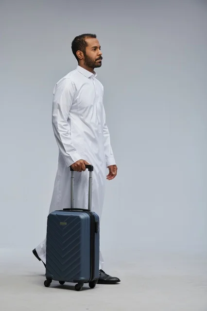 Saudi Man in White Thobe Walking with Blue Suitcase