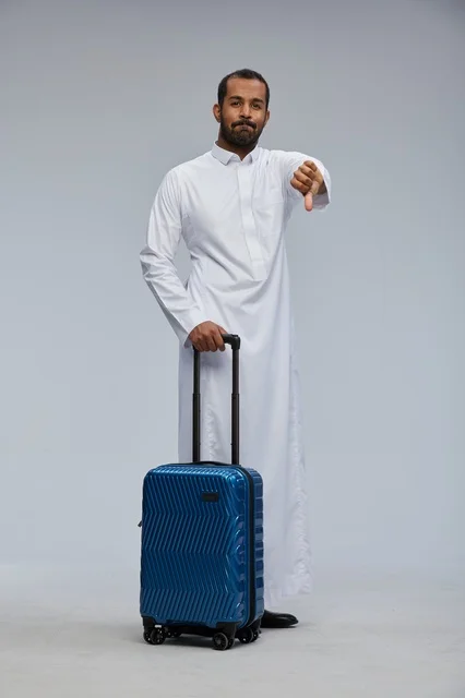 رجل سعودي يحمل حقيبة سفر زرقاء مع إيماءة رفض وإحباط
