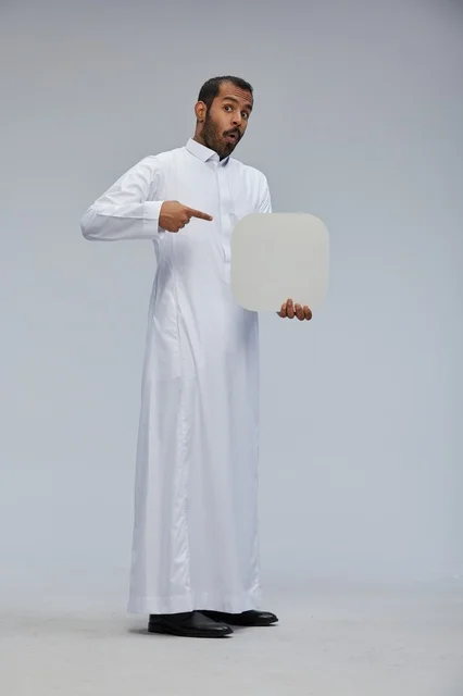 رجل سعودي يرتدي الثوب يحمل لوحة بيضاء فارغة بتعبير مندهش
