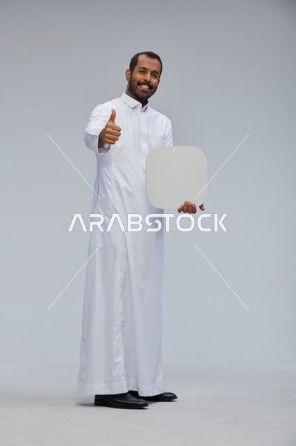 رجل سعودي يرتدي الثوب يحمل لوحة بيضاء فارغة وإشارة إعجاب