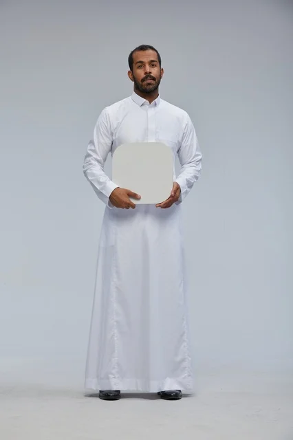 رجل سعودي يرتدي الثوب يحمل لوحة بيضاء فارغة في استوديو