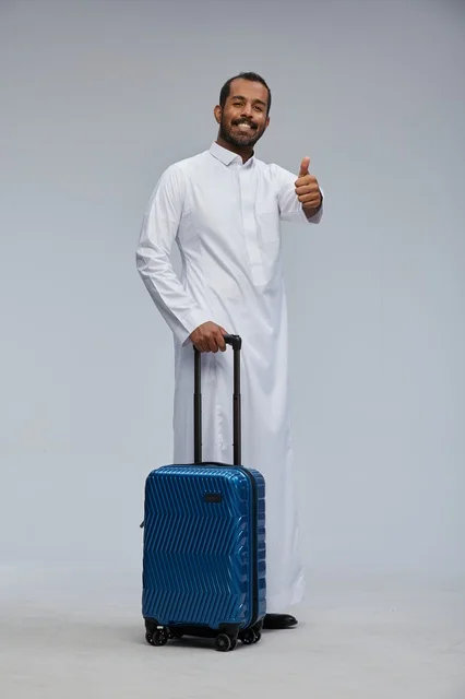 رجل سعودي مسافر مع حقيبة سفر زرقاء بالثوب