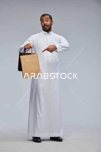 رجل سعودي يرتدي الثوب الأبيض يحمل كيس تسوق