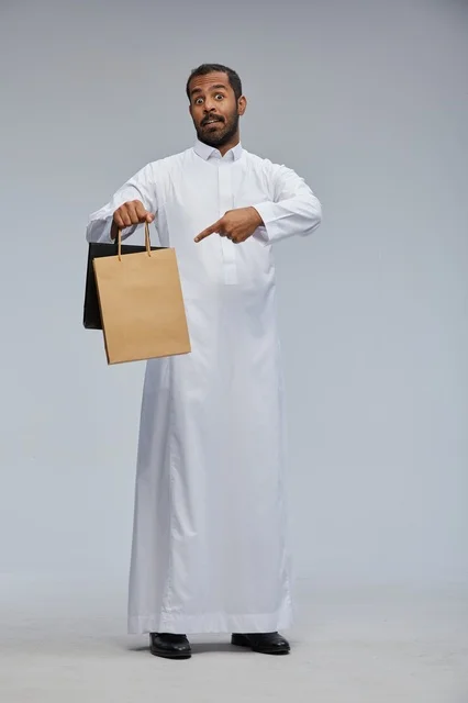 رجل سعودي يرتدي الثوب الأبيض يحمل كيس تسوق