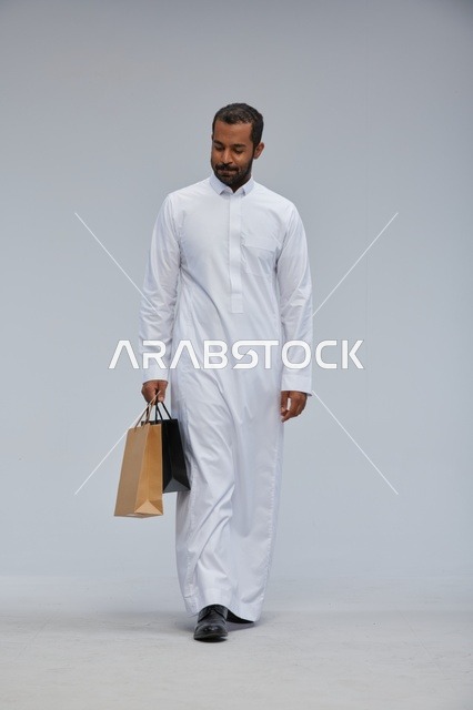 Saudi Man in White Thobe Carrying Shopping Bags in Studio