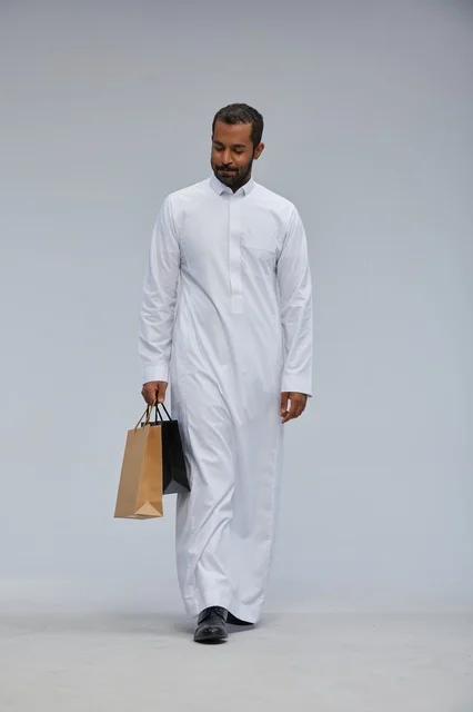 رجل سعودي يرتدي الثوب الأبيض ويحمل أكياس التسوق
