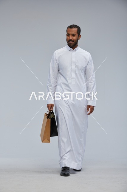 رجل سعودي بالثوب الأبيض يحمل أكياس تسوق