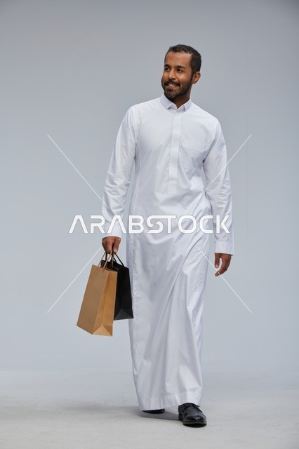 رجل سعودي بالثوب الأبيض يحمل أكياس تسوق في الاستوديو