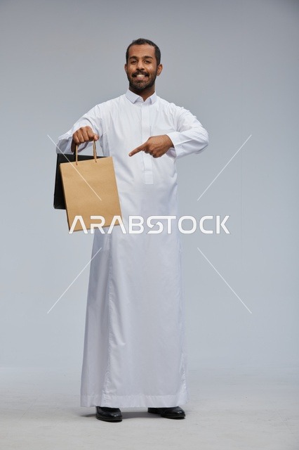 رجل سعودي بالثوب الأبيض يحمل أكياس تسوق