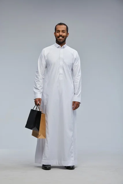 رجل سعودي يرتدي الثوب الأبيض ويحمل أكياس تسوق ملونة