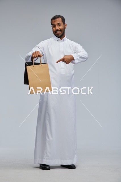 رجل سعودي بالثوب التقليدي يحمل أكياس تسوق